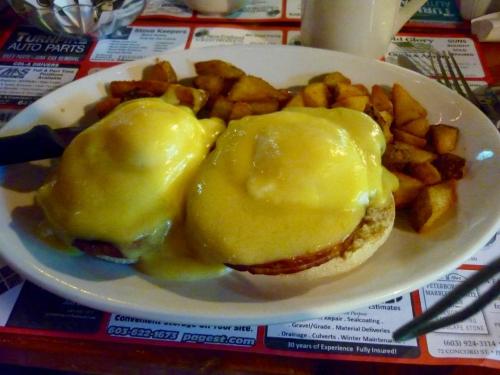 A plate of eggs Benedict with two poached eggs and hollandaise sauce, served with golden-brown potato wedges.