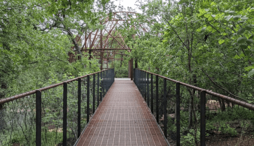 A wooden bridge leads through lush greenery to a partially constructed dome structure in the background.