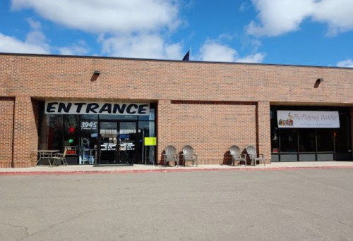 Exterior view of a brick building with a large "ENTRANCE" sign and two chairs outside. Clear blue sky above.