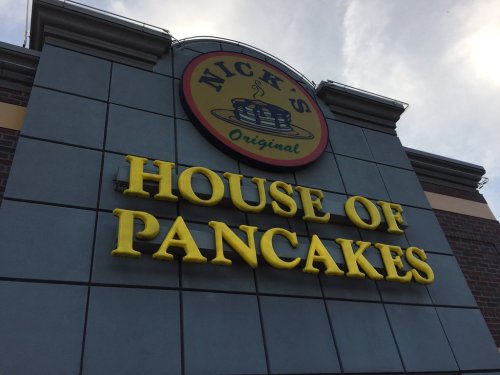 Sign for "Nick's House of Pancakes" with a yellow logo and text against a gray building.