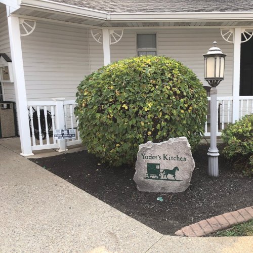 Sign for Yoder's Kitchen next to a bush and a lamp post, in front of a white building.