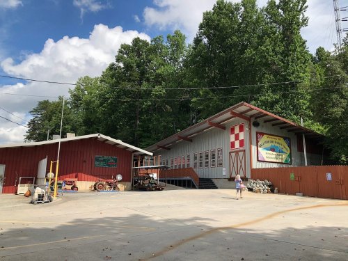 A rustic building with red and white accents, surrounded by trees, featuring a sign and outdoor space.