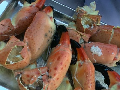 A platter of large, cooked crab claws with orange and black shells, some partially cracked open.