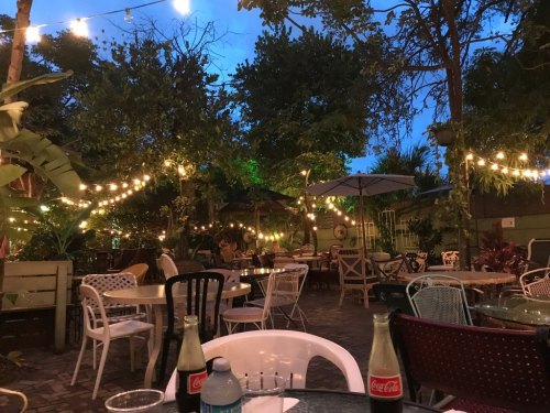 A cozy outdoor dining area with string lights, tables, and chairs surrounded by trees at dusk.