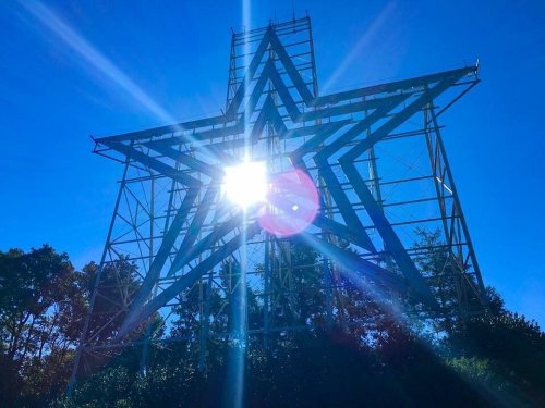 A large star structure shines brightly against a clear blue sky, with sunlight creating a lens flare effect.