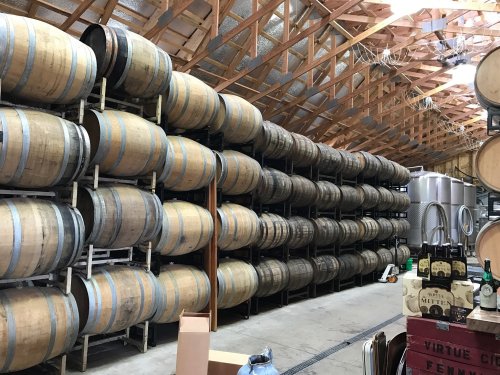 A spacious winery interior featuring stacked wooden barrels and metal fermentation tanks.