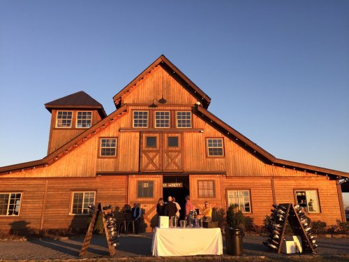 A rustic wooden barn at sunset, with people gathered around a table outside.