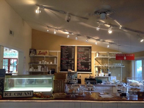 A cozy café interior with a display case, menu board, and signs for ice cream and ordering. Brightly lit and inviting.