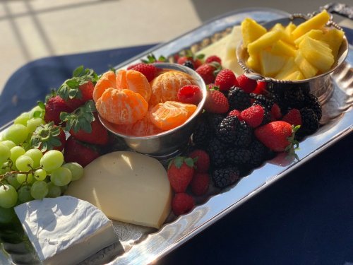 A silver platter filled with assorted fruits, including grapes, strawberries, and pineapple, alongside cheese.