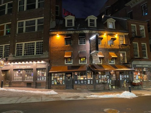A historic brick building at night, featuring warm lights, awnings, and a cozy atmosphere, with snow on the ground.