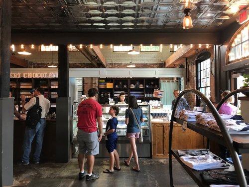 A cozy chocolate shop with customers browsing and a display of treats, featuring warm lighting and rustic decor.