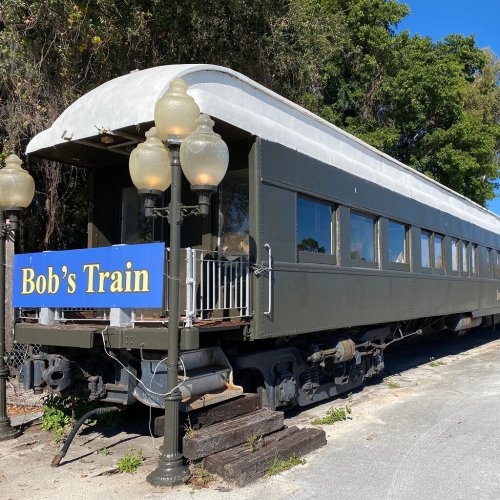 A vintage train car named "Bob's Train" parked beside a pathway, surrounded by greenery and street lamps.