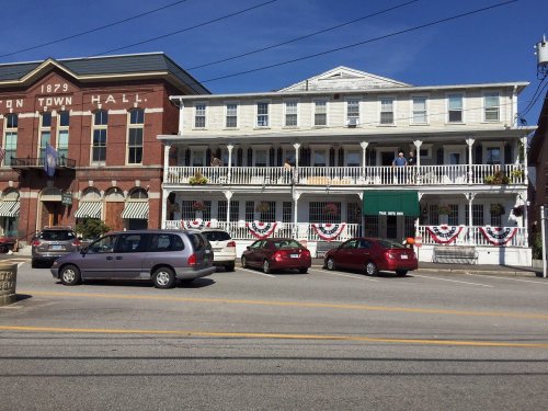 Historic buildings with decorative bunting, featuring a town hall and a multi-story porch, set against a clear blue sky.