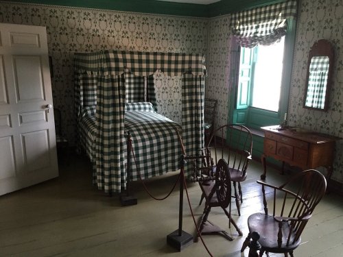 A vintage bedroom with a checkered canopy bed, wooden furniture, and patterned wallpaper.