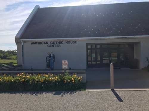 Exterior of the American Gothic House Center, featuring a sign and a garden with flowers in front.