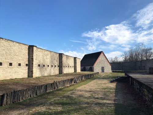 A stone fort with a red-roofed building, surrounded by grassy areas and blue skies with scattered clouds.