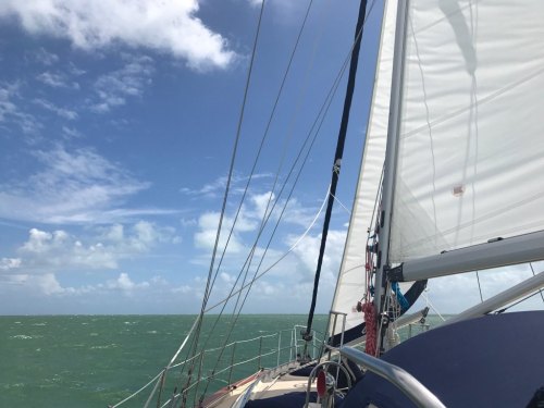 A sailboat on calm waters, with a clear blue sky and fluffy clouds in the background.