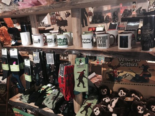 A display of various mugs, socks, and merchandise featuring playful designs and slogans on wooden shelves.