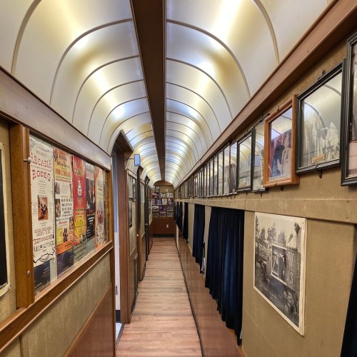 A long, narrow hallway lined with framed photos and posters, illuminated by soft overhead lighting.