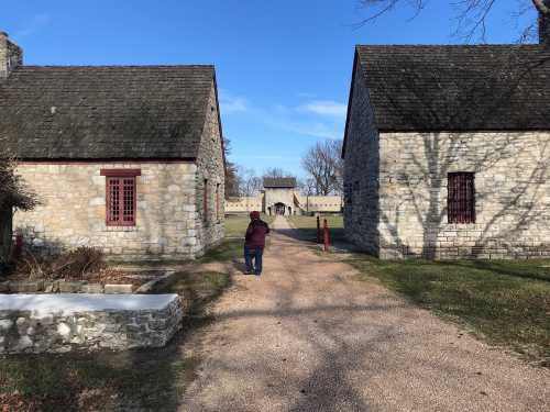 A person walks down a gravel path between two stone buildings on a clear day.