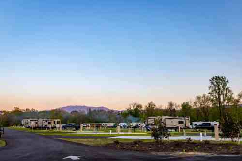 A scenic RV park at dusk, with several RVs lined up along a winding road and mountains in the background.