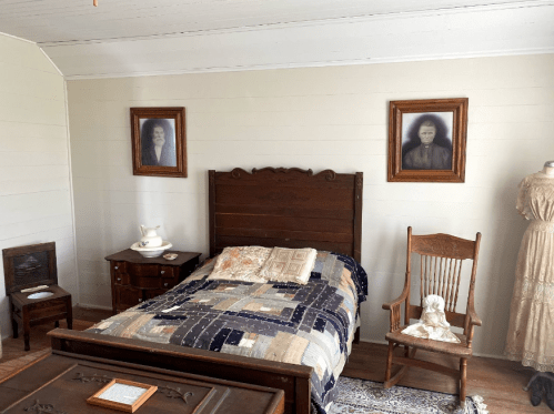 A cozy bedroom featuring a wooden bed, quilt, rocking chair, and vintage portraits on the walls.