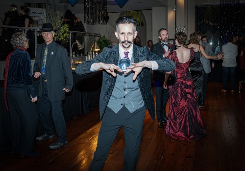 A man in a suit holds a crystal ball, surrounded by elegantly dressed guests at a lively event.