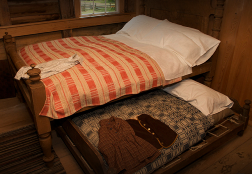 A wooden bunk bed with a red and white striped blanket on top and a patterned blanket on the bottom, with clothes draped over.