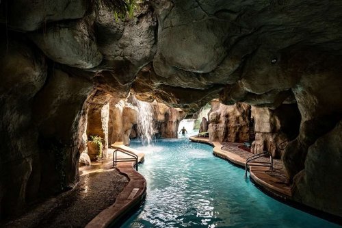 A serene cave-like pool area with waterfalls and lush greenery, inviting relaxation and tranquility.