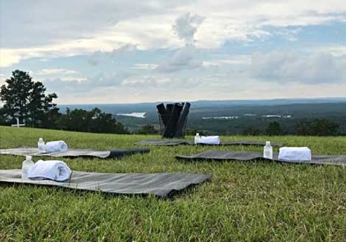 Yoga mats and towels set up on grass, overlooking a scenic view of hills and a river under a cloudy sky.