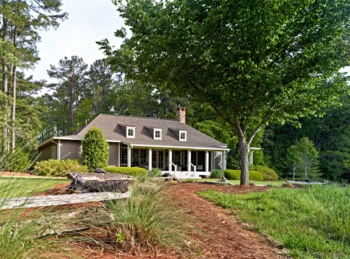 A charming house surrounded by greenery, featuring a porch and large trees in a serene outdoor setting.