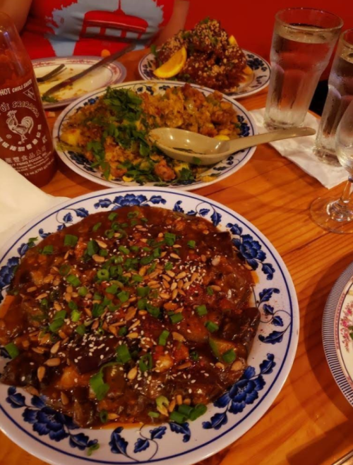 Three colorful plates of food on a wooden table, featuring a savory dish with green onions and sesame seeds.