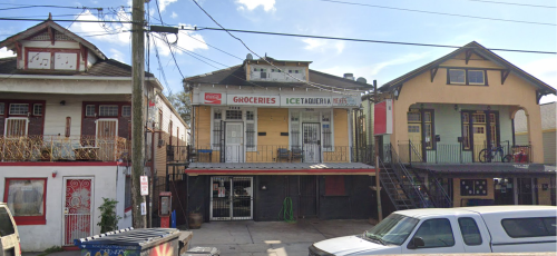 A row of colorful houses with a grocery store in front, featuring balconies and a clear blue sky.