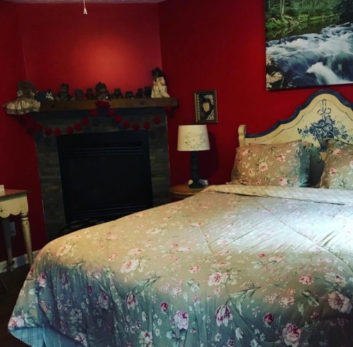 Cozy bedroom with a floral bedspread, red walls, a fireplace, and a bedside lamp.