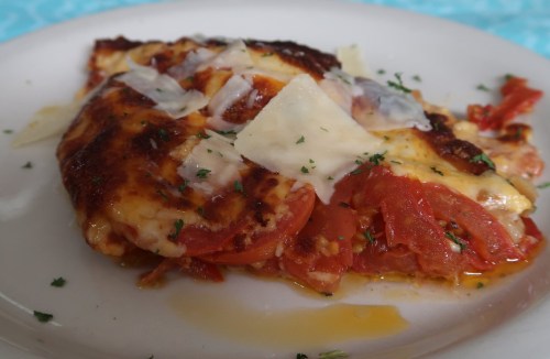 A slice of baked lasagna with layers of tomatoes, cheese, and herbs on a white plate.