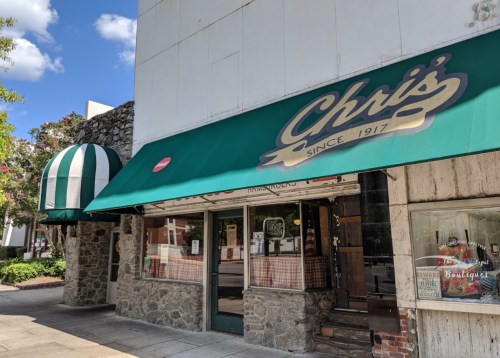 Exterior of Chris's restaurant, featuring a green awning and stone facade, with a striped canopy on the side.