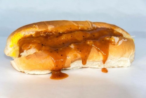 A hot dog in a bun topped with a thick, brown sauce, resting on a white surface.