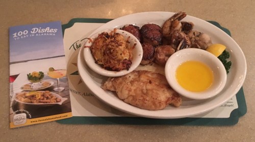 A plate of seafood featuring fried fish, shrimp, crab cakes, and a side of lemon and dipping sauce, with a menu nearby.