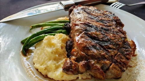 A plate featuring a grilled steak with green beans and creamy mashed potatoes, garnished with sauce.