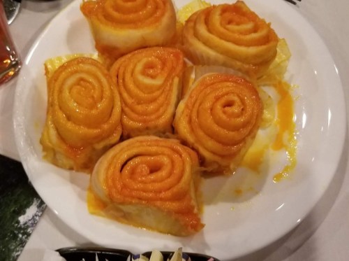 A plate of six golden, spiral-shaped pastries with a glossy orange glaze, arranged neatly on a white dish.