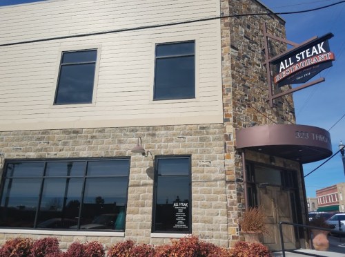 Exterior of All Steak Restaurant, featuring a stone facade and large windows, with a sign above the entrance.