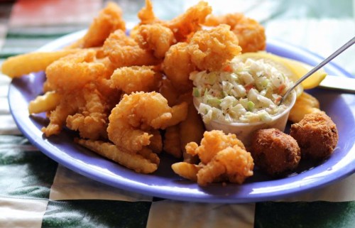 A plate of fried shrimp, coleslaw, hushpuppies, and French fries on a blue platter.