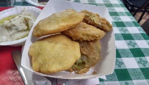 A tray of golden, crispy fried pastries, some filled with green vegetables, on a checkered tablecloth.