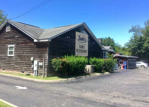 A rustic wooden building with a sign reading "Zack's Family Restaurant," surrounded by greenery and a clear blue sky.