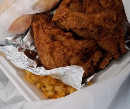 A takeout container with crispy fried chicken, macaroni and cheese, and two soft rolls wrapped in paper.