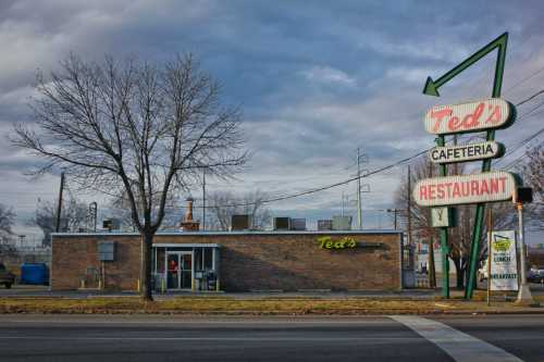 A brick building with a sign reading "Ted's Cafeteria Restaurant" under a cloudy sky, with trees nearby.