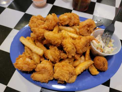 A blue plate filled with crispy fried shrimp, crinkle-cut fries, coleslaw, and a hushpuppy on a checkered table.