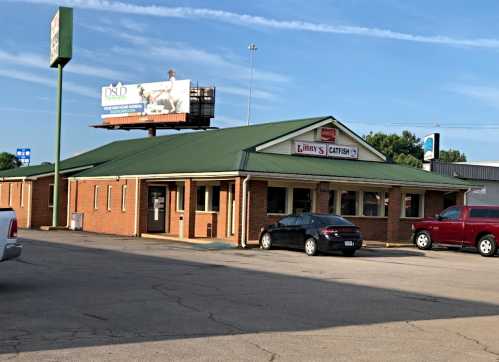 A brick restaurant with a green metal roof, featuring a sign for "J. R.'s Catfish" and a billboard in the background.