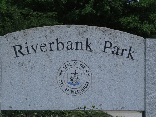 Sign for Riverbank Park featuring the city seal of Westbrook, surrounded by greenery.