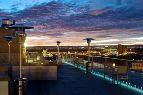 Rooftop terrace at dusk, featuring outdoor seating, heaters, and a panoramic view of the city skyline under a colorful sky.